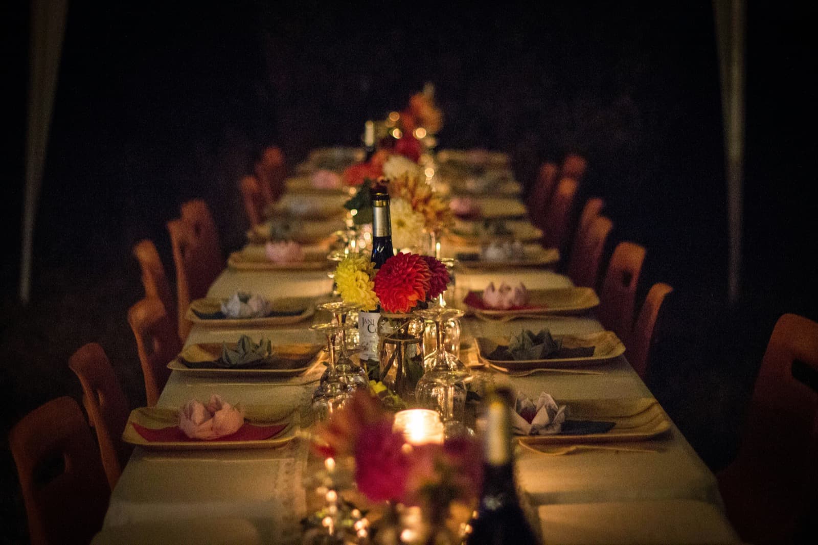 A long banquet table set for an evening event, candlelit with flowers and place settings
